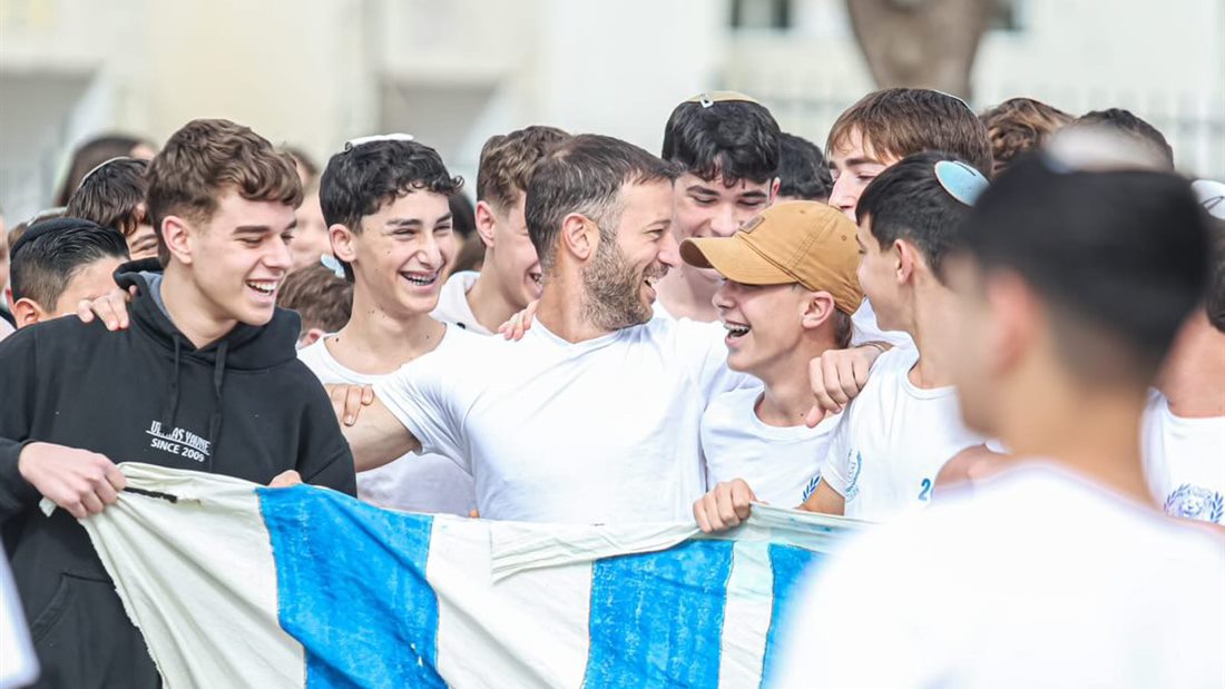 שבי צוחק עם אוהדים צעירים של יבנה שמחזיקים דגל